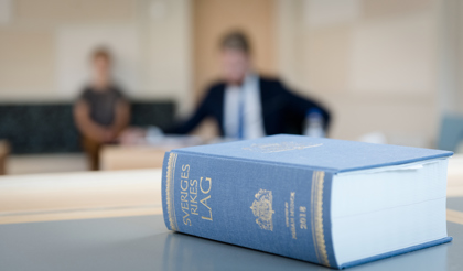 Bild på en lagbok som ligger på ett bord. Två suddiga personer i bakgrunden. 