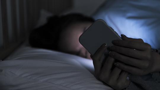 Ung person i en säng som tittar på sin mobil. Foto: shih-wei/iStock