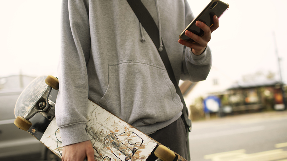 Ung person med skateboard som tittar på sin mobil. Foto: Caiaimage/Johnér