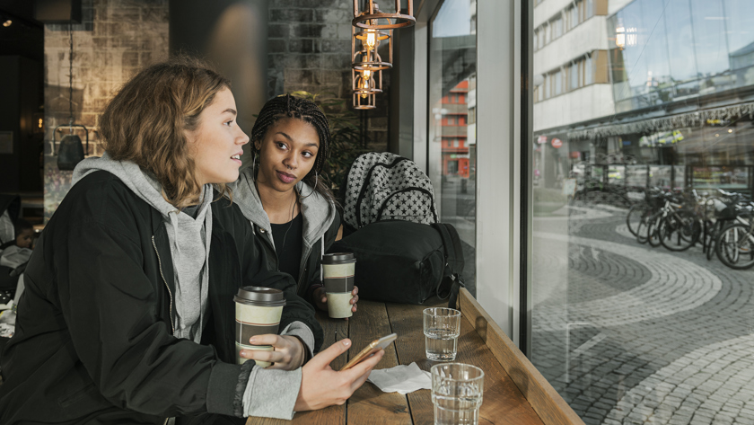 Två tjejer samtalar med varandra på ett café.
